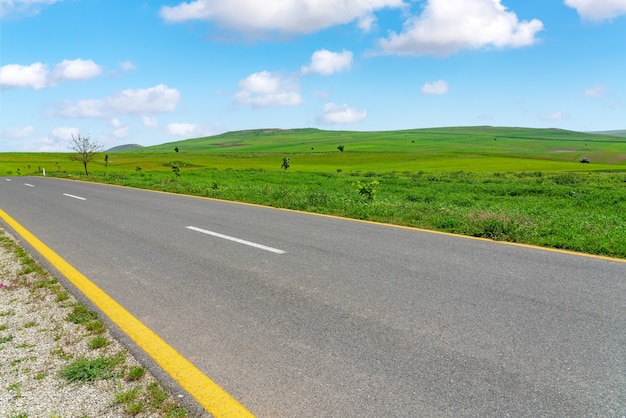 Carretera asfaltada entre campos agrícolas verdes con cielo azul y nubes