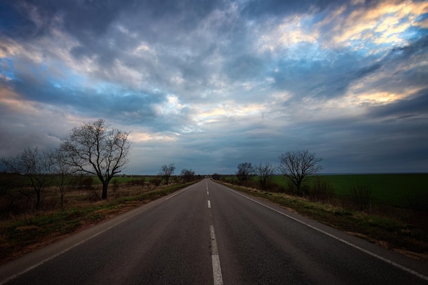 Carretera asfaltada de noche vacía al atardecer Árboles y prados verdes