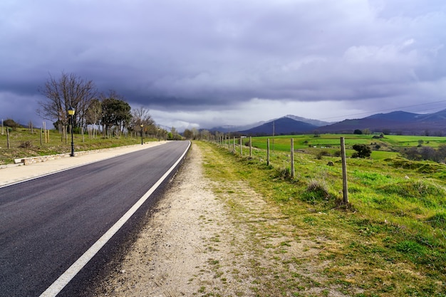 Carretera asfaltada que conduce a las montañas con cielo oscuro de nubes de tormenta. Madrid.