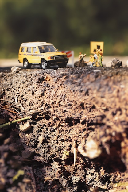 Carretera de asfalto agrietada y obras viales con figuras en miniatura en un entorno campestre. Enfoque suave y composición de profundidad de campo superficial.