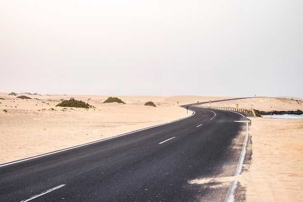 Carretera de asfalto negro oscuro en medio del desierto y dunas de arena.