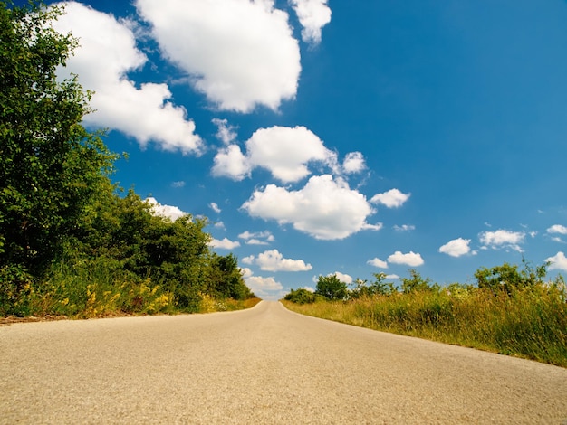 Carretera de campo paisaje al aire libre y cielo con nubes sol de verano y fondo en la naturaleza Asfalto de la calle y primavera con maquetas de árboles y plantas desde un ángulo bajo en un entorno natural