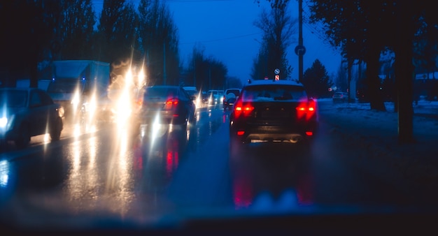 Carretera de la ciudad de la noche a través de los coches de parabrisas gota de agua de fondo abstracto en las luces de cristal y la lluvia.