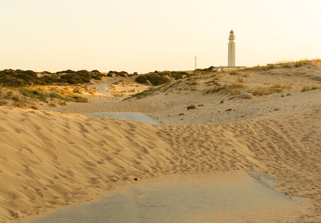 Carretera cubierta de arena desde las dunas, camino hacia el faro de Trafalgar, Cádiz, España al atardecer