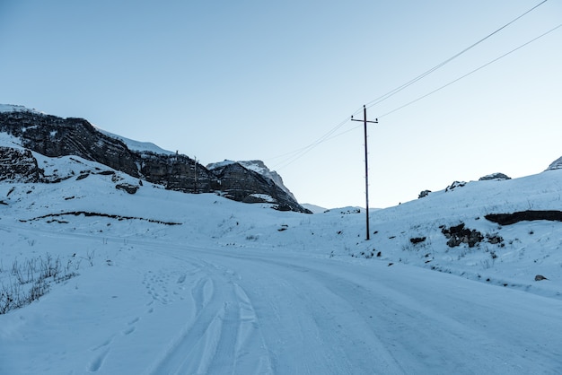 Carretera cubierta de nieve en las montañas, postes de energía a lo largo de la carretera