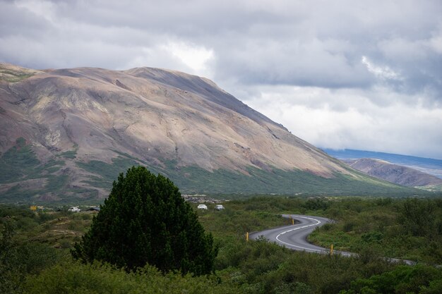 Carretera de curva en S cerca de la colina con árbol verde y cielo en Islandia.