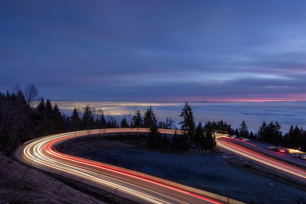 Carretera que sube una montaña y niebla que cubre la ciudad moderna