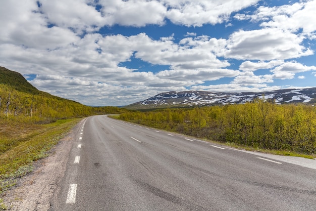 Carretera recta y solitaria entre montañas suecas bajo un cielo nublado