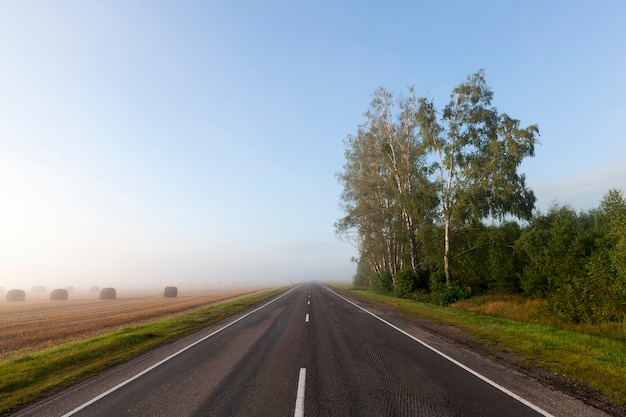 Una carretera separada en la temporada de la mañana, frente a una gran niebla, a los lados del bosque y el campo agrícola.