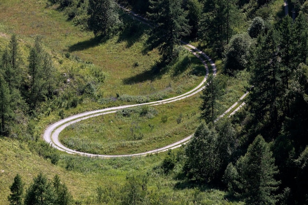 Carretera a través de las montañas altas montañas y un bosque verde en un cálido día de verano en cada lado Hola