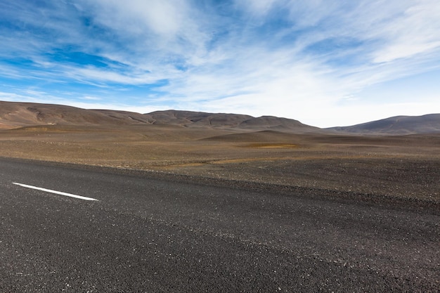 Carretera a través del paisaje de campo de lava de grava seca bajo un cielo azul de verano