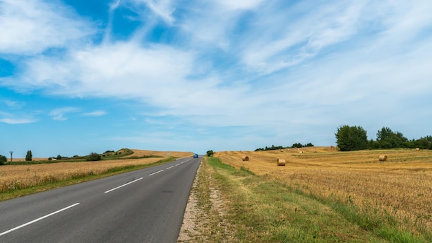 Una carretera vacía fuera de la ciudad pasa por un campo rural y un prado floreciente Viaje en automóvil lejos de la ciudad y el ajetreo Camino pavimentado en un día soleado sin automóviles