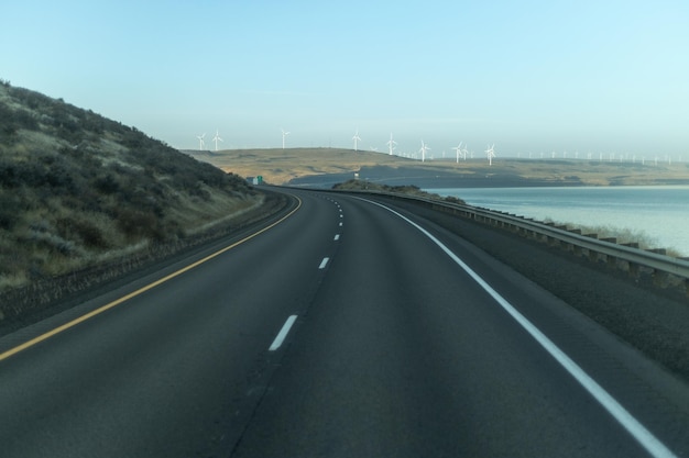 Carretera con vista al mar y un parque eólico a lo lejos.