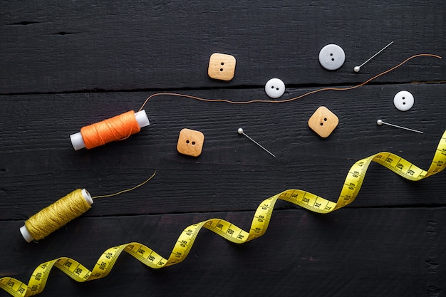 Carretes de hilo de colores, alfileres, cinta métrica y botones para coser sobre una superficie de madera marrón