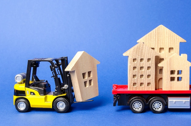 Una carretilla elevadora amarilla carga una figura de madera de una casa en un concepto de transporte de camión