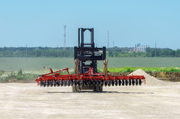 Carretilla elevadora transporta grada de discos. El cargador se desplaza sobre un sitio de tierra. Equipo de transporte.