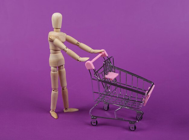 Carretilla de supermercado de rollos de marionetas de madera sobre fondo púrpura Concepto de compras