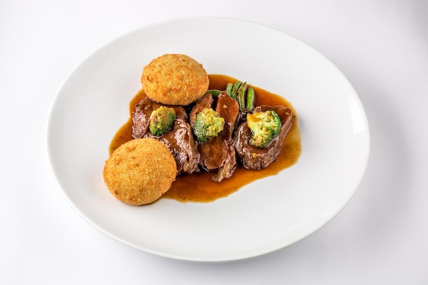 Carrilleras de cerdo en salsa con brócoli y judías verdes en una placa blanca.