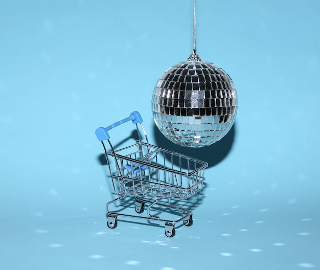 Carrinho de compras com bola de discoteca em fundo azul brilhante conceito de festa minimalista