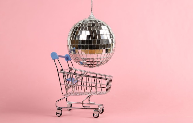 Carrinho de compras com bola de discoteca em um fundo rosa Conceito de festa minimalista