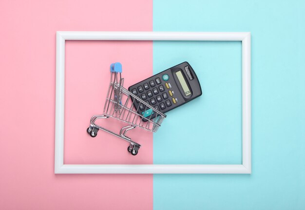 Carrinho de compras com calculadora em uma moldura branca em uma superfície rosa pastel