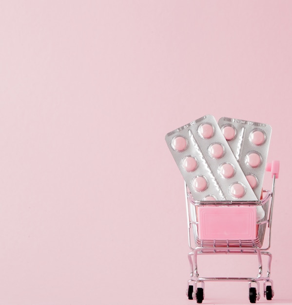 Carrinho de compras com comprimidos médicos na parede rosa com espaço de cópia