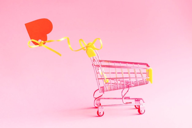 Carrinho de compras com coração em fundo rosa Promoção e modelo de compras Espaço da cópia do dia dos namorados em tons