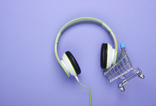 Carrinho de compras com novos fones de ouvido estéreo na superfície roxa