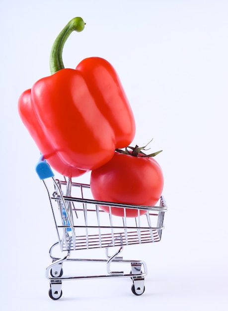 Carrinho de compras com pimentão e tomate em um branco