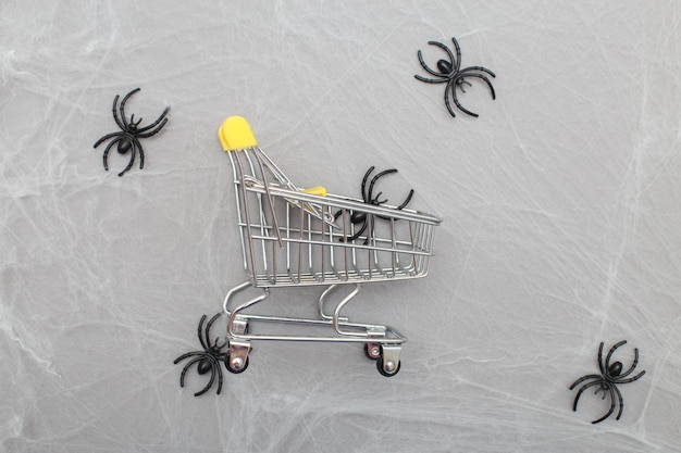 Carrinho de compras com teia de aranha e aranhas em um fundo cinza conceito de compras de halloween