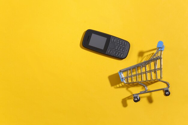 Carrinho de compras com telefone com botão em fundo amarelo. vista do topo