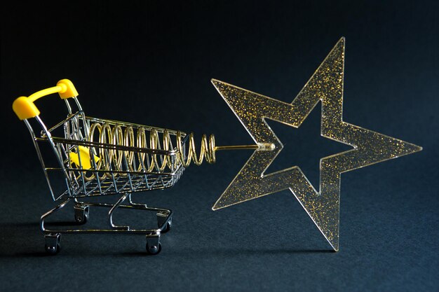Foto carrinho de compras com uma estrela transparente dourada com lanternas na forma de uma árvore de natal em um fundo preto black friday comprando presentes para o ano novo espaço para texto