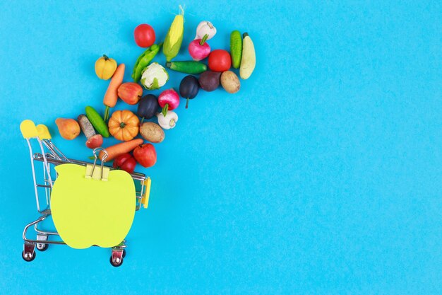 Carrinho de compras de metal com frutas e vegetais em um fundo azul Carrinho de compras em miniatura de brinquedo