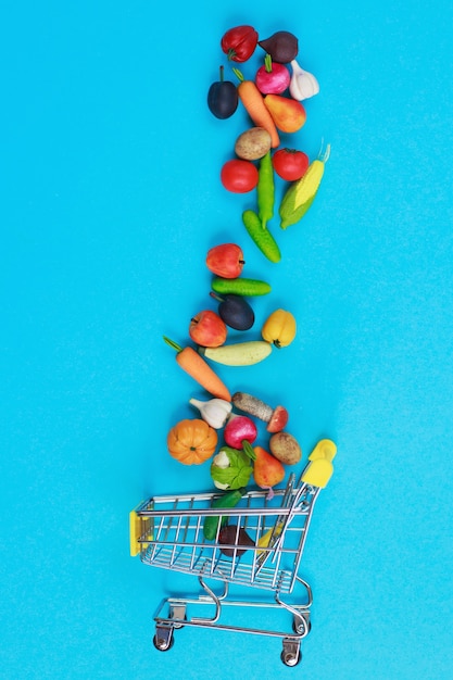 Carrinho de compras de metal com frutas e vegetais em um fundo azul. Carrinho de compras em miniatura de brinquedo