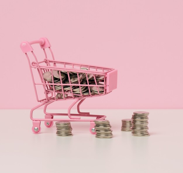 Carrinho de compras de metal em miniatura e uma pilha de moedas em uma mesa branca. O conceito de descontos e vendas, economia de orçamento. Comércio online