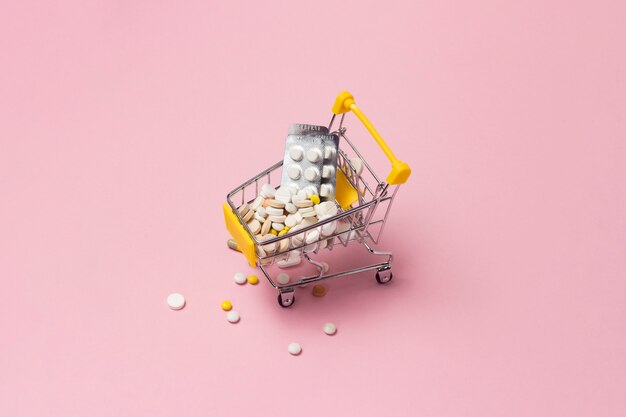Carrinho de compras do supermercado cheio de comprimidos e drogas em um fundo rosa. Compras de medicamentos, compra na Internet.