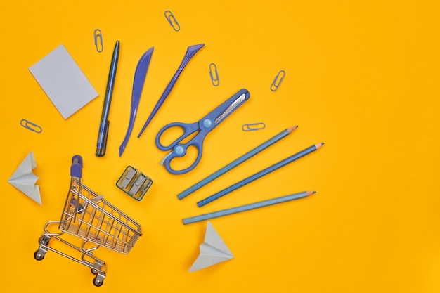 Foto carrinho de compras e artigos de papelaria do minimalismo em fundo amarelo