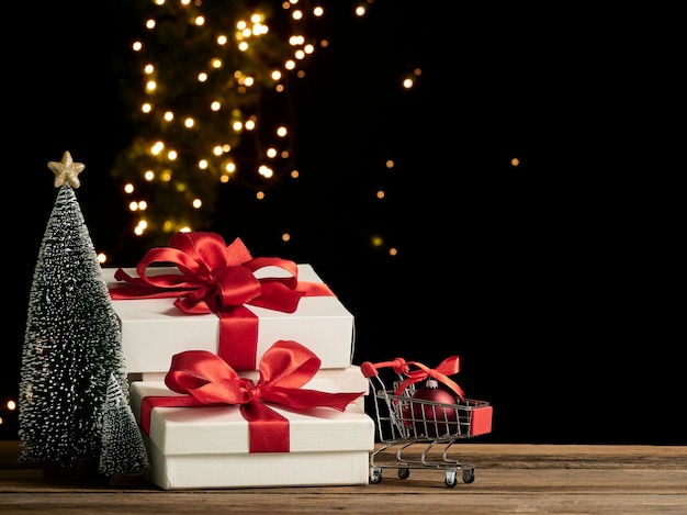 Carrinho de compras e caixas de presente de Natal na mesa de madeira, espaço para texto
