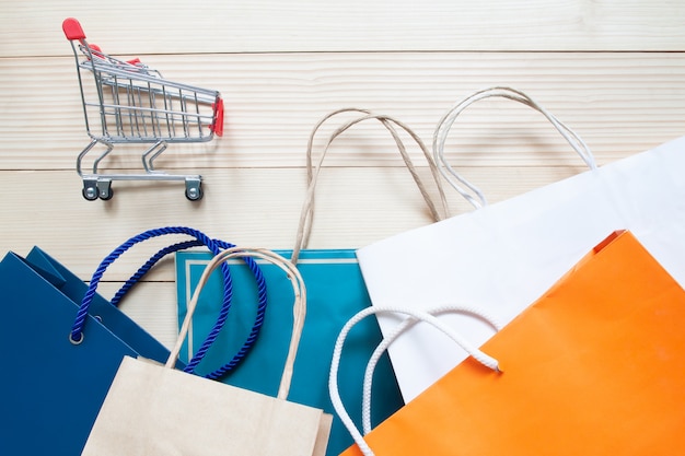 Carrinho de compras e sacolas multicolour em fundo de madeira