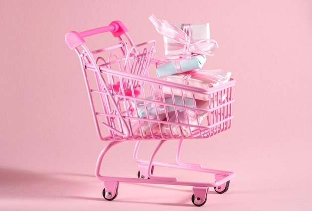 Carrinho de compras Ping cheio de caixas de presentes cor-de-rosa e azul em fundo rosa
