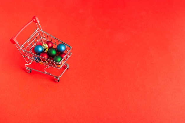 Carrinho de compras sobre rodas com enfeites de natal em fundo vermelho