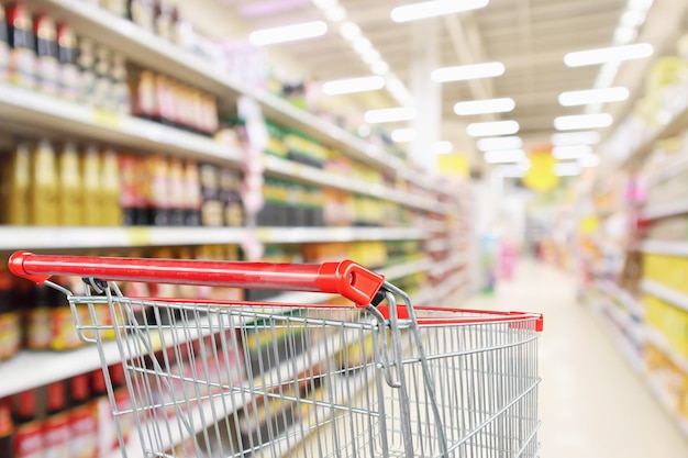 Foto carrinho de compras vazio com desfoque abstrato de supermercado loja de desconto corredor e molho de temperos prateleiras de produtos interior fundo desfocado