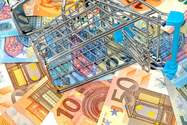 Foto carrinho de compras vazio invertido nas notas de euro. conceito de cesta de alimentos de alto custo ou poder de compra
