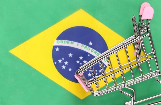 Carrinho de mini supermercado no fundo desfocado da bandeira do brasil. conceito de compras.