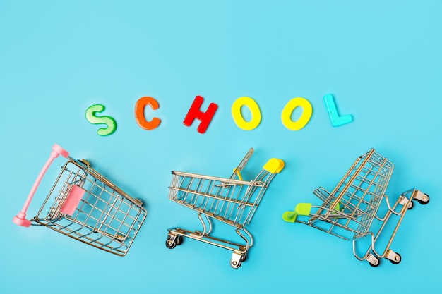 Carrinhos de carrinhos de compras vazios e a palavra escola de letras multicoloridas em um fundo azul Conceito para uma loja de mercadorias para escola e educação Conceito de venda e desconto