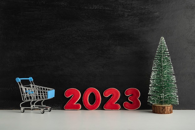Carrito de árbol de Navidad y números 2023 sobre fondo oscuro Compras para el Año Nuevo Espacio de copia