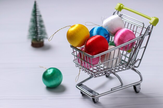 Carrito y coloridas bolas de año nuevo, árbol de Navidad, compras planas