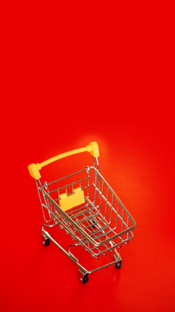 Foto carrito de la compra amarillo pequeño vacío sobre fondo rojo. copie el espacio, coloque el texto. venta de concepto. foto vertical