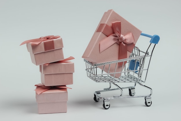 Carrito de la compra y cajas de regalo con arcos sobre fondo blanco. Composición para navidad, cumpleaños o boda.