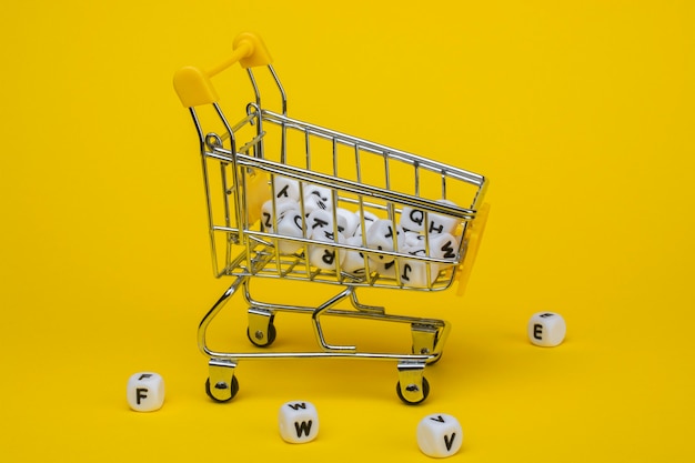 Carrito de la compra y cubos con letras sobre un fondo amarillo